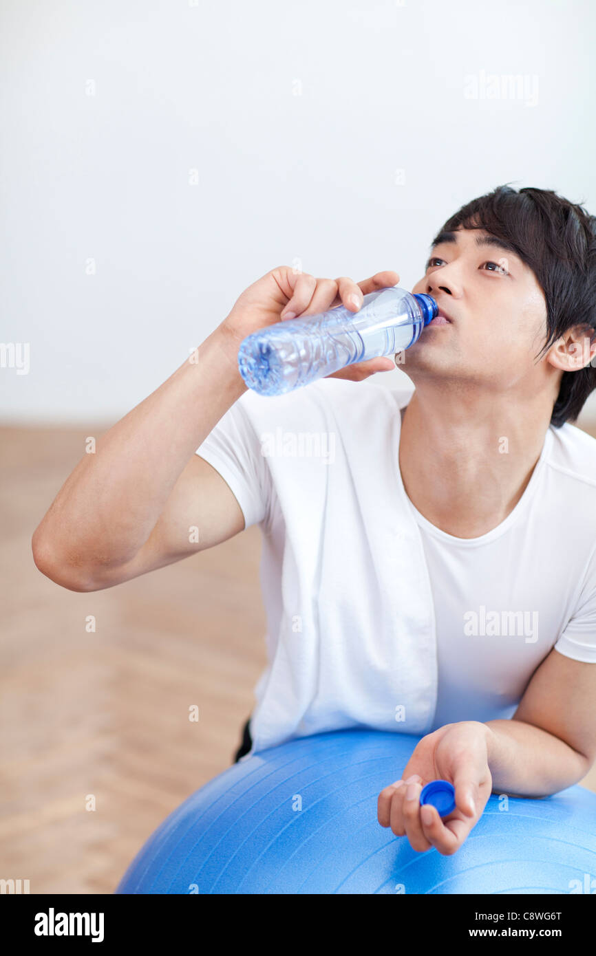 Asiatischer Mann stützte sich auf Pilates Ball trinken Wasser aus Flasche Stockfoto