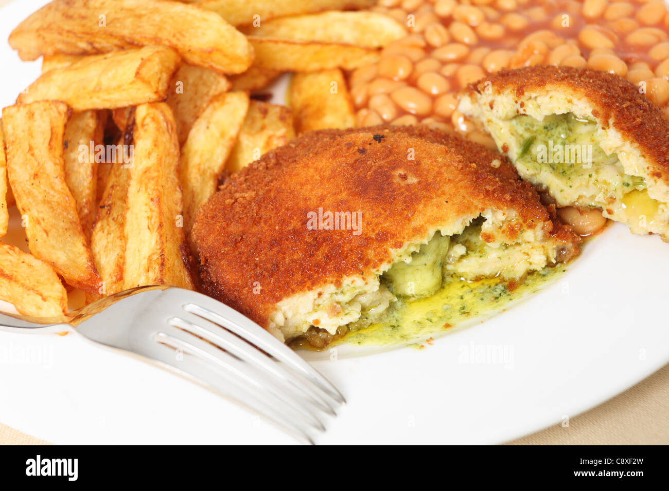 Ein Huhn Kiew zeigen die Knoblauchbutter und Petersilie füllen, close-up mit gebackenen Bohnen und einer Gabel. Stockfoto