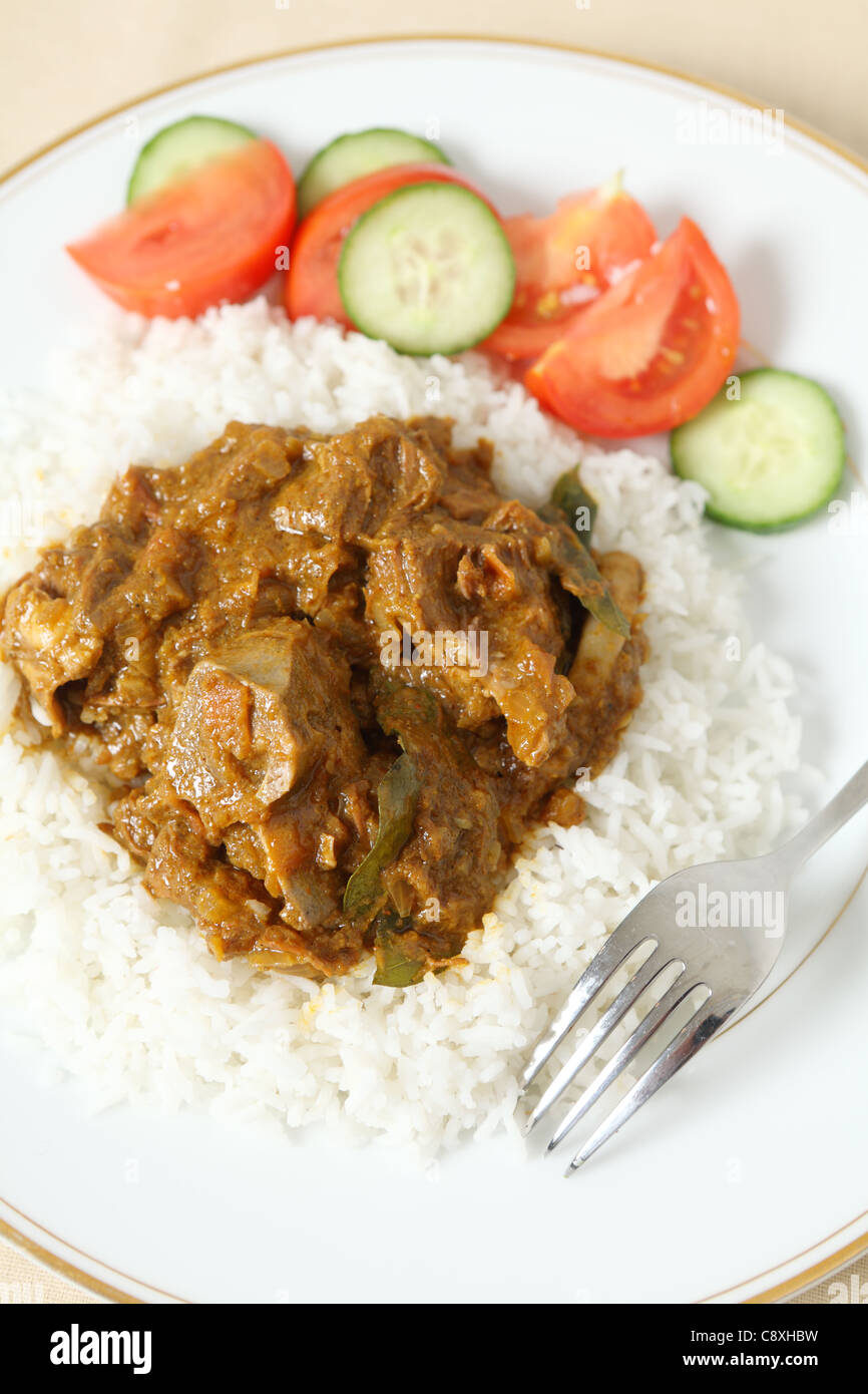Lamm Rogan Josh, mit Basmati-Reis und einem Salat aus Tomaten und Gurken. Das Lamm, am Knochen ist in einer würzigen Tomatensauce. Stockfoto