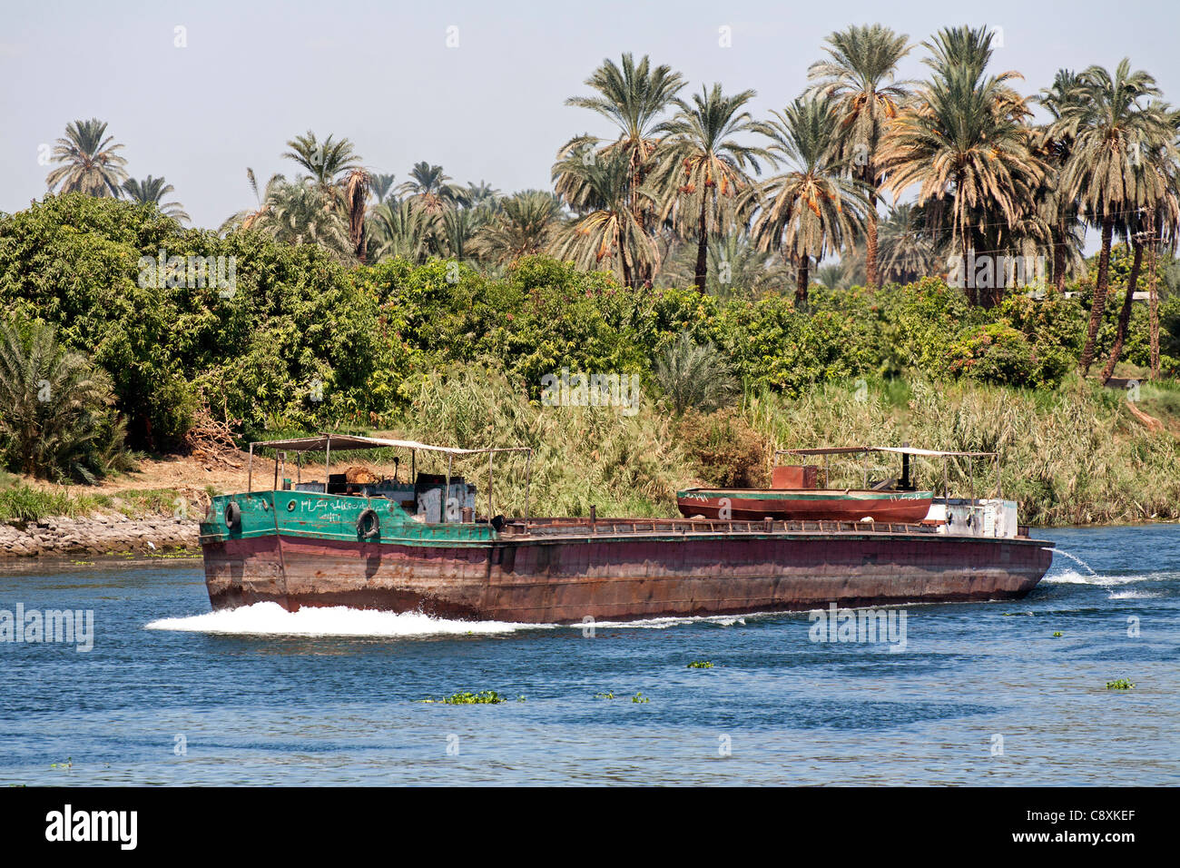 Ein Teil der Nil mit Schlepper Boot Segeln in Richtung Kamera mit Palmen und Bäumen am Ufer des Flusses hinter Ägypten Stockfoto