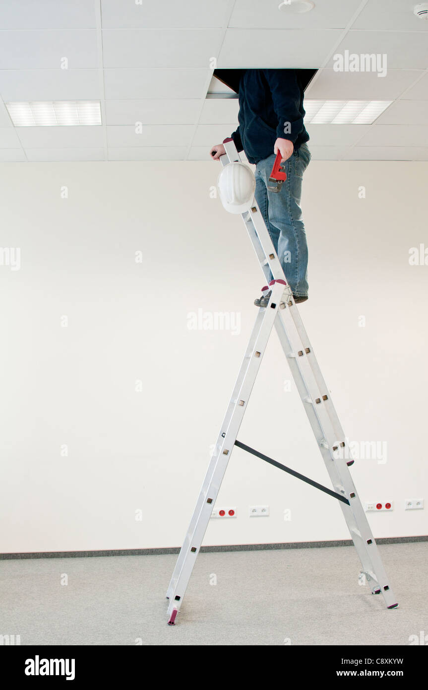 Mann auf einer Leiter mit einem hydraulischen Schraubenschlüssel, Blicke über die Decke Stockfoto