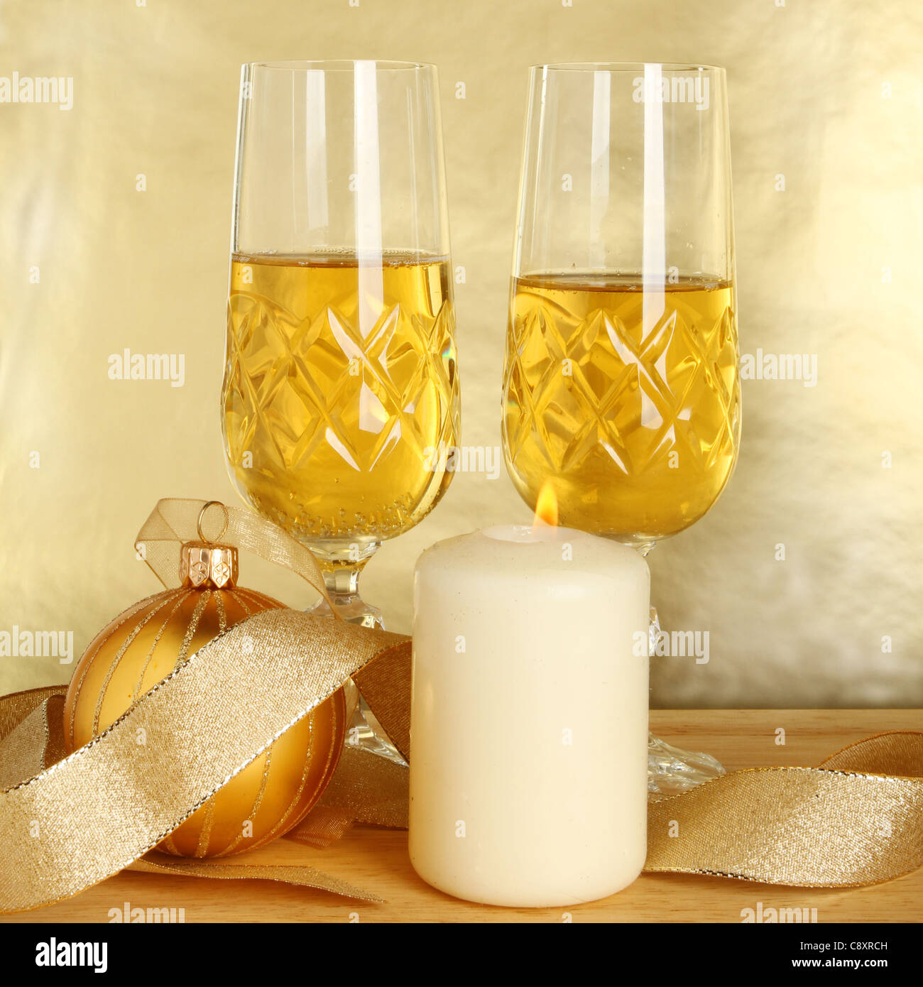 Zwei Gläser Champagner, Goldband und Weihnachtskugel mit einer brennenden Kerze auf einem goldenen Hintergrund Stockfoto