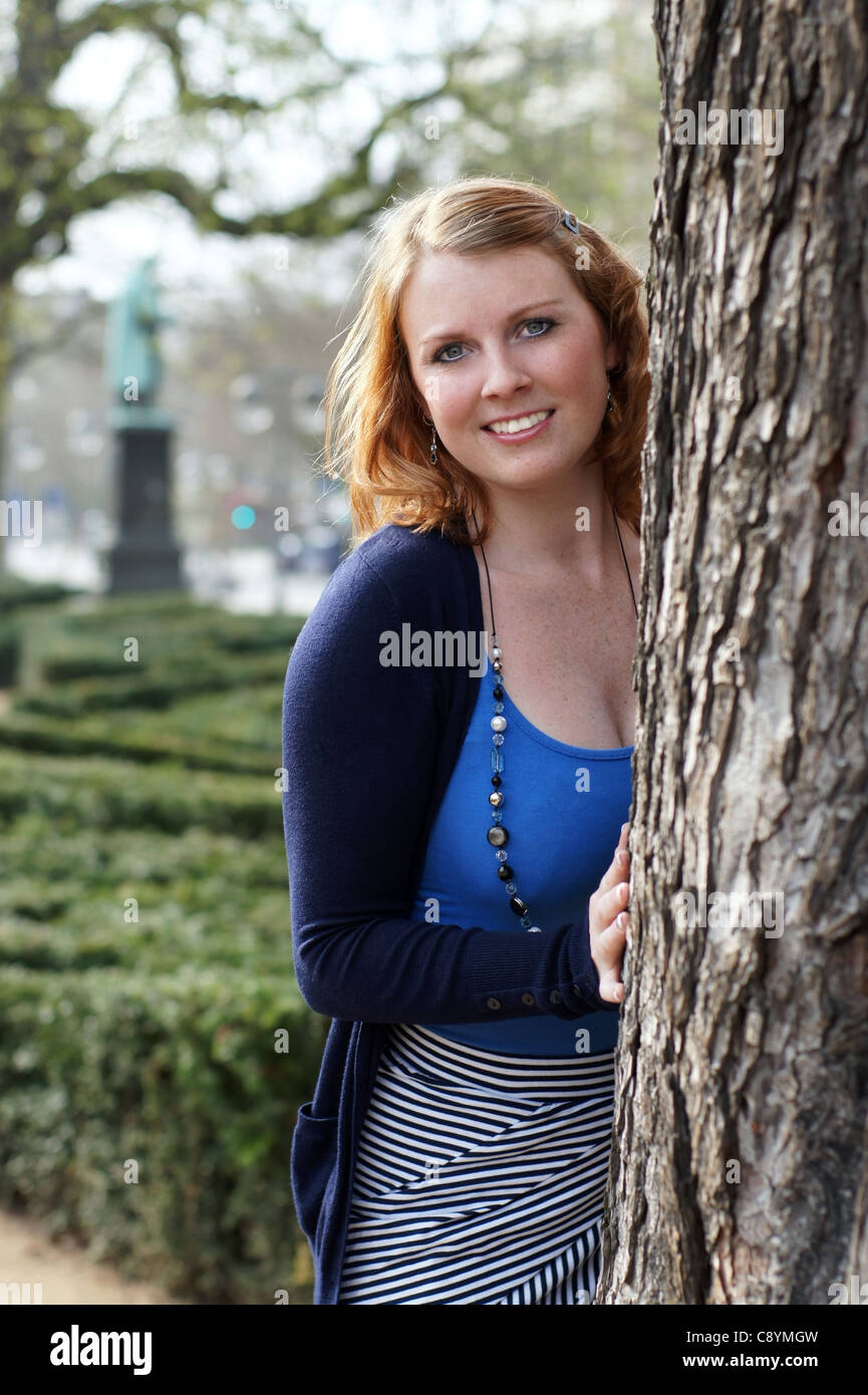 lächelnde junge Frau hinter Baum Stockfoto