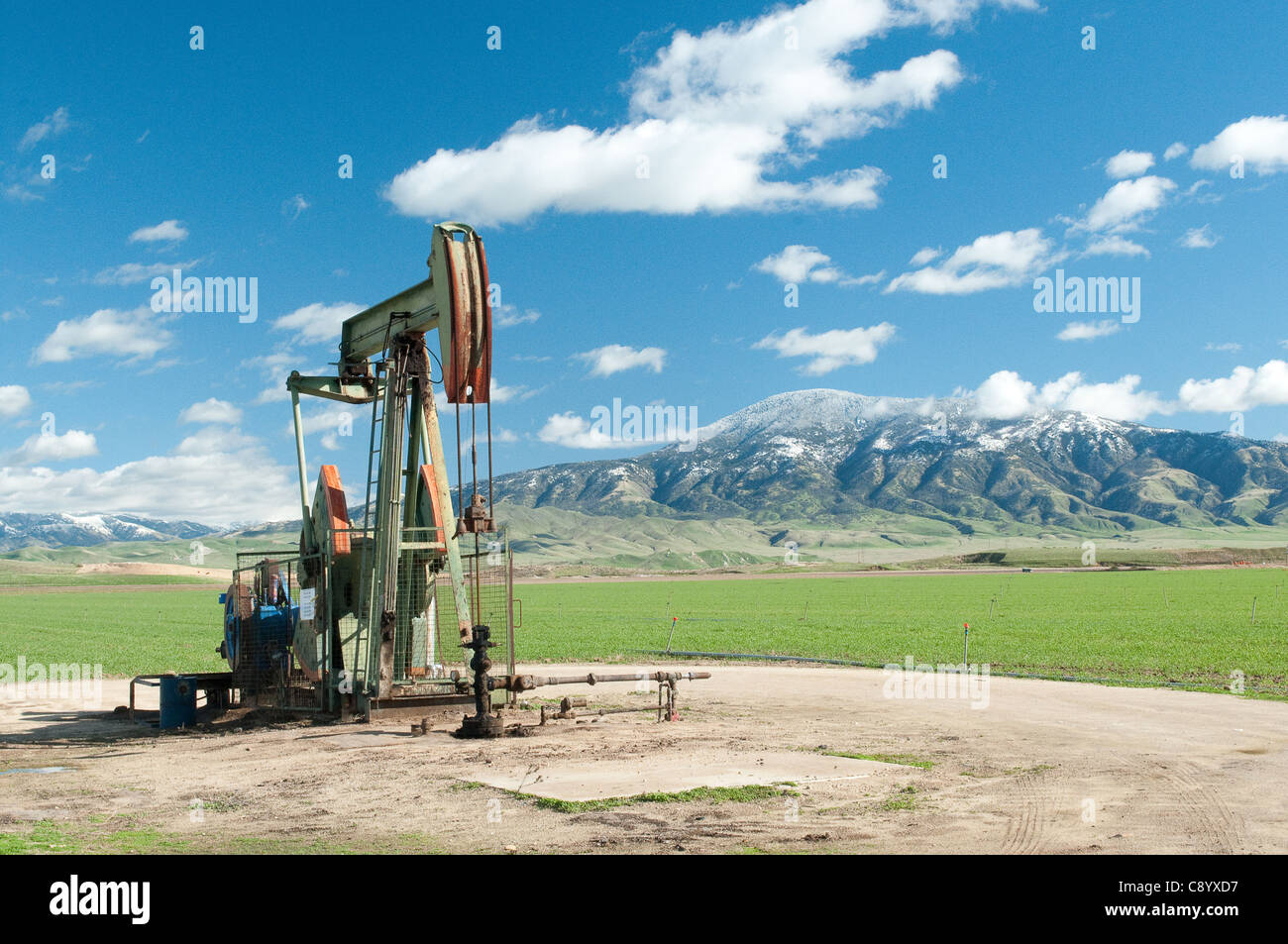 Oil Derrick außerhalb Bakersfield mit Schnee bedeckt Berge und Wiesen im Hintergrund.  Gute Darstellung von sauberer Energie Stockfoto