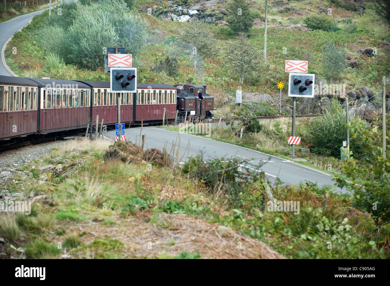 2 ft. Schmalspur Dampf Lok double Fairlie "Merddin Emrys" zieht seinen Zug über einen Bahnübergang über eine Straße auf dem Weg zu Porthmadog auf die wieder-Bahn verläuft zwischen Porthmadog und Blaenau Ffestiniog, Snowdonia, North Wales, UK. Stockfoto