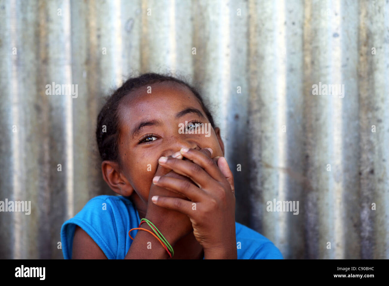 Ein schüchternes junges Mädchen mit dunklen schwarzen Augen Lächeln auf den Lippen, aber ihr Lächeln mit ihren Händen in Hell-Ville, Nosy Be, Madagaskar versteckt Stockfoto