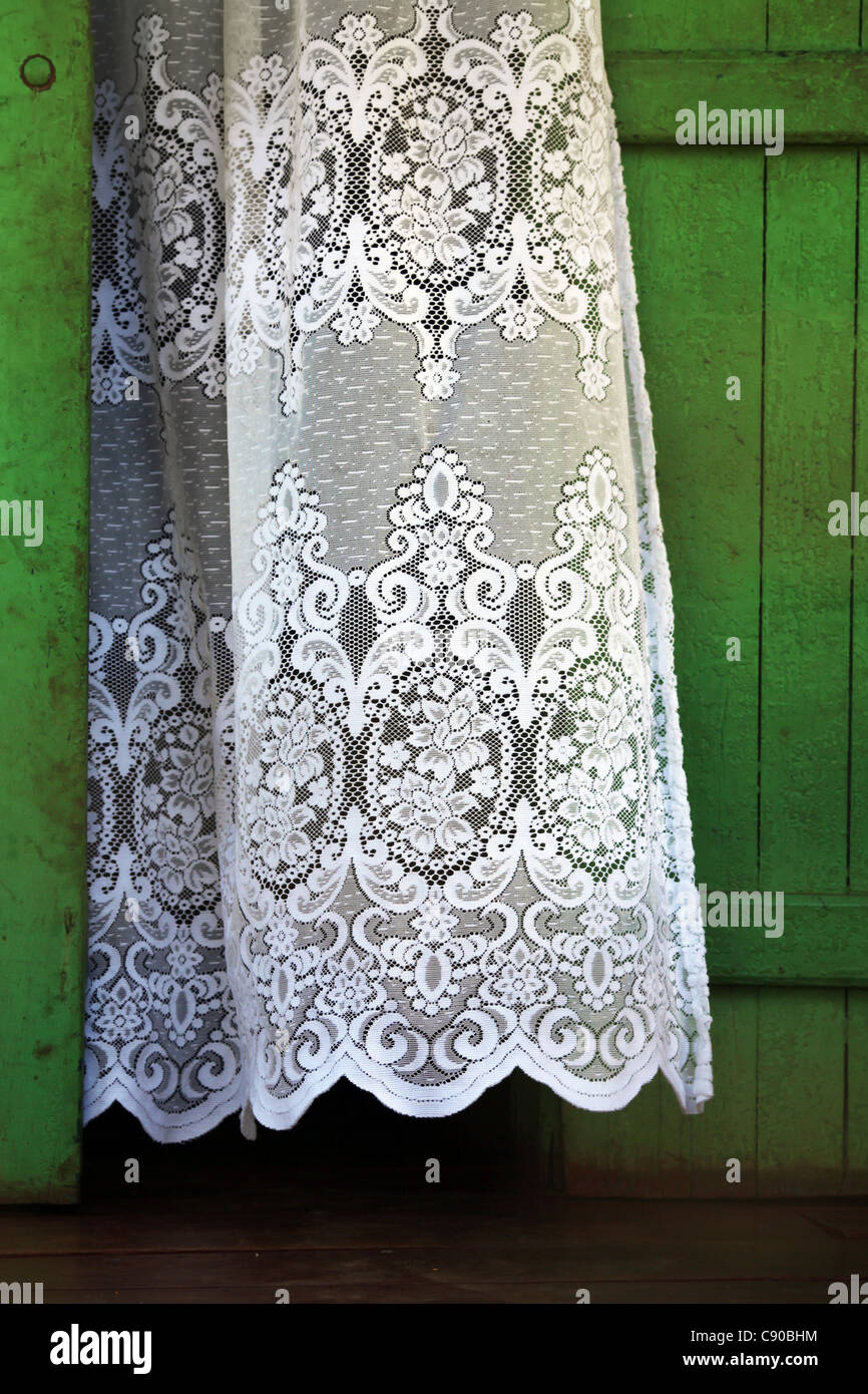 Einen weißen bestickten Vorhang fließt in die Brise neben einem grünen Holztür in Hell-Ville, Nosy Be, Nossi-Bé, Madagaskar. Stockfoto