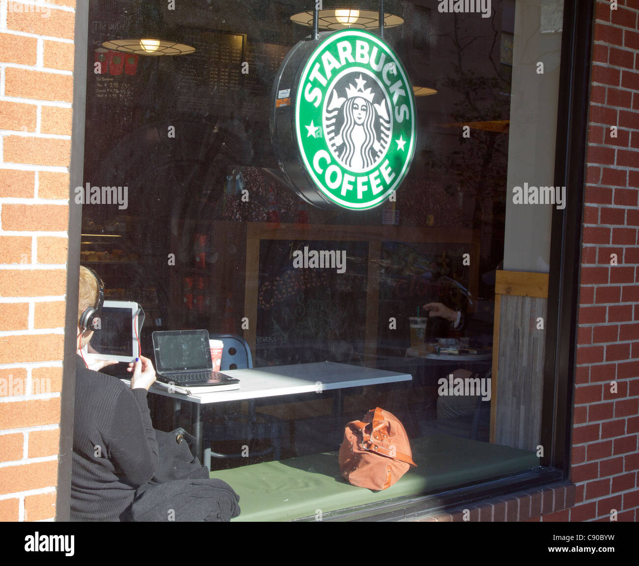 Ein junger Mann sitzt neben einem Starbuck Fenster in Brooklyn, New York Stockfoto