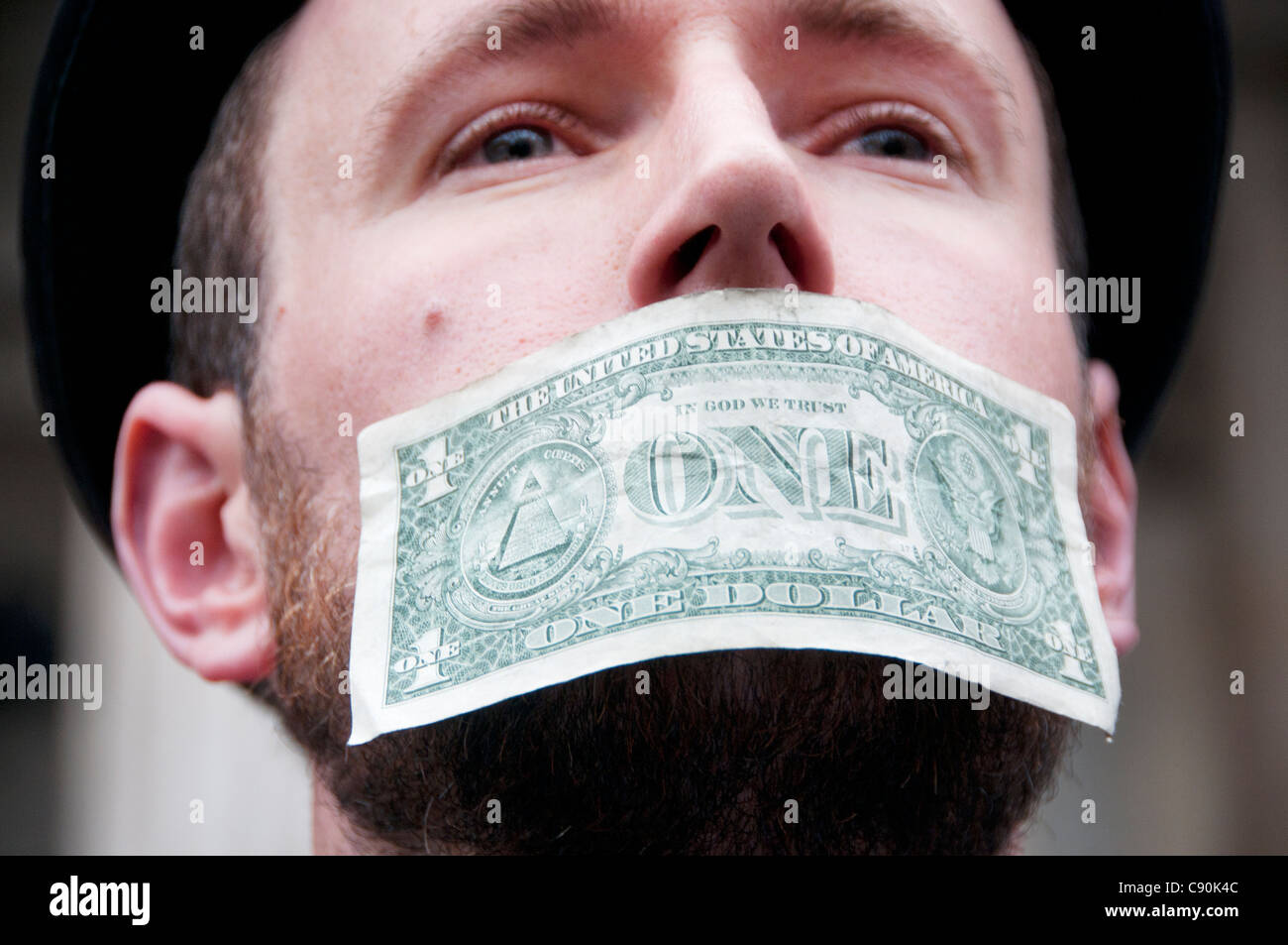 London zu besetzen. St. Pauls. Protest gegen die Stadt und den Banken. Demonstrant mit einer Dollarnote zum Mund stecken Stockfoto