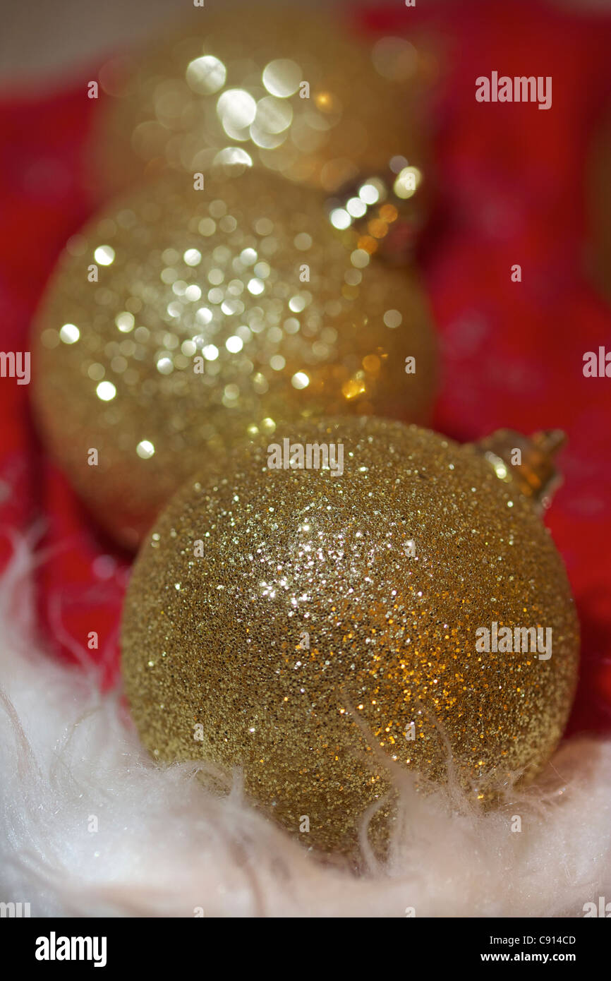 Drei Gold farbig funkelnden Christbaumkugeln am roten und weißen Hintergrund. Weißes Fell im Vordergrund, konzentrieren sich auf vorderen Christbaumkugel Stockfoto