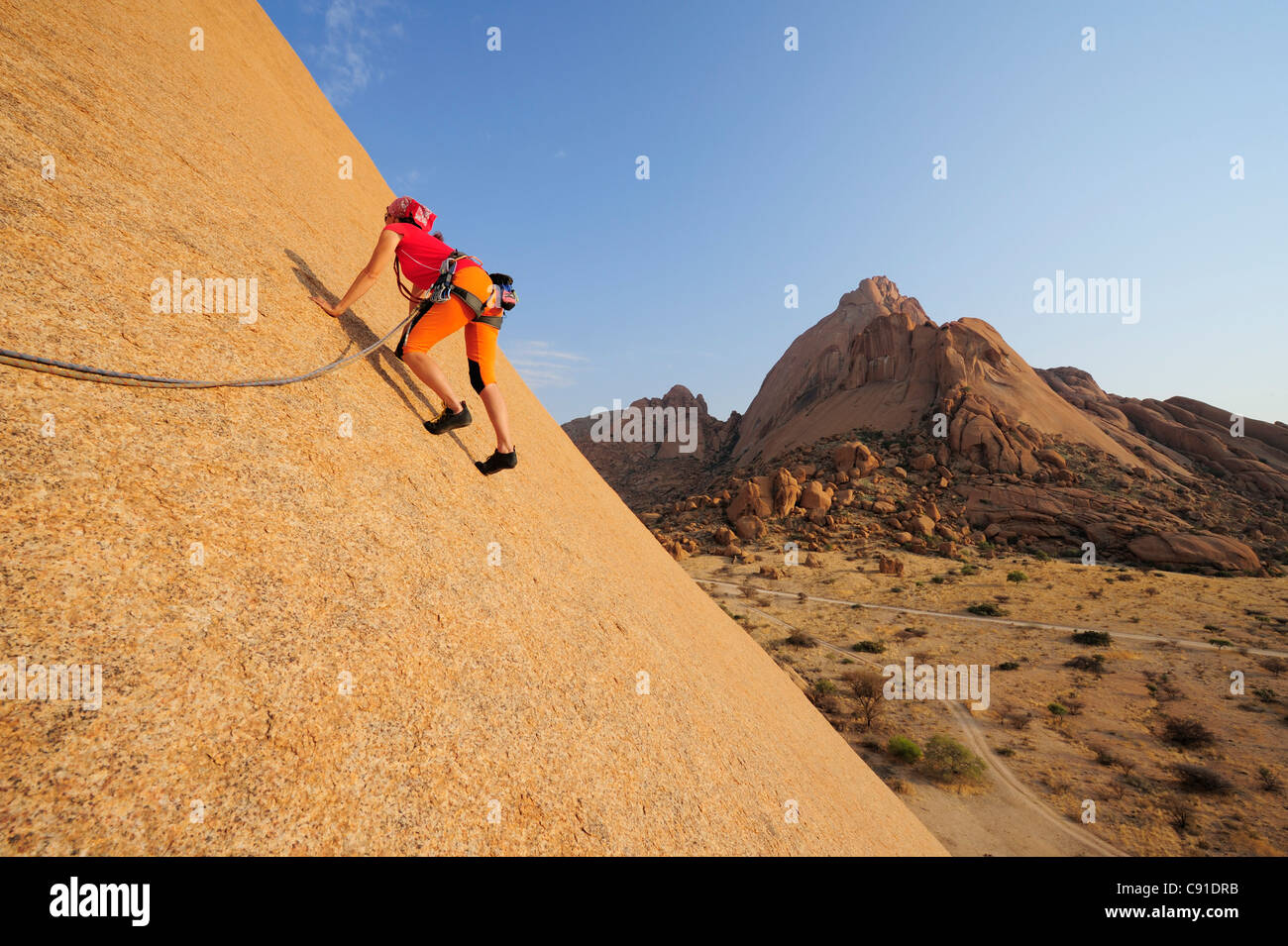 Frau Klettern am roten Felswand, große Spitzkoppe im Hintergrund, große Spitzkoppe, Namibia Stockfoto