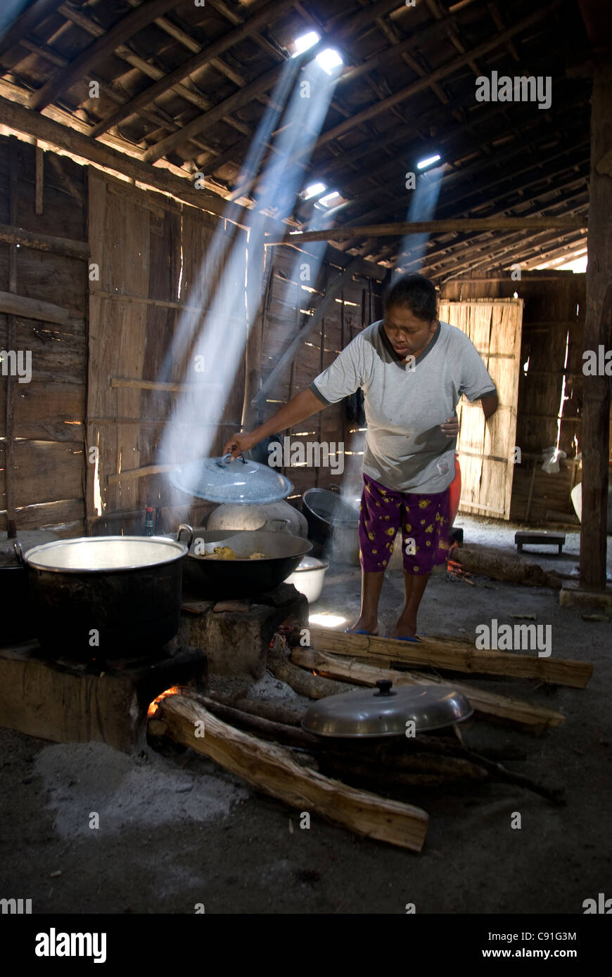Frau in der Hütte, die in Töpfen auf einem offenen Holzofen kocht, wobei Sonnenlicht durch das Dach kommt, Dorf Randublatung, in der Nähe von CEPU, Zentral-Java, Indonesien Stockfoto