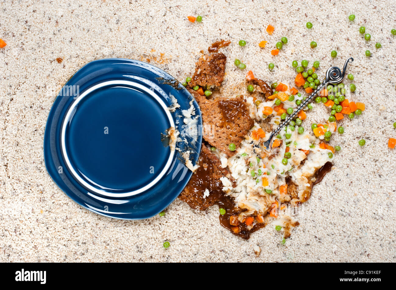 Ein Teller mit Hackbraten mit Kartoffelpüree und Erbsen fiel auf neuen Teppich. Stockfoto