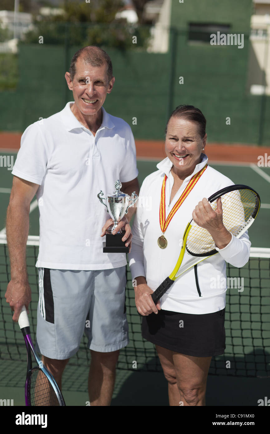 Älteres Ehepaar mit Trophäe auf Tennisplatz Stockfoto