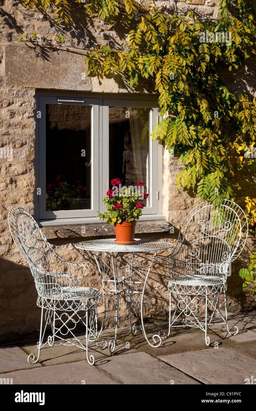 Metall Gartenstühle und Tisch mit Topfpflanze vor Haus auf steinernen Terrasse im englischen Garten Stil Französisch Stockfoto