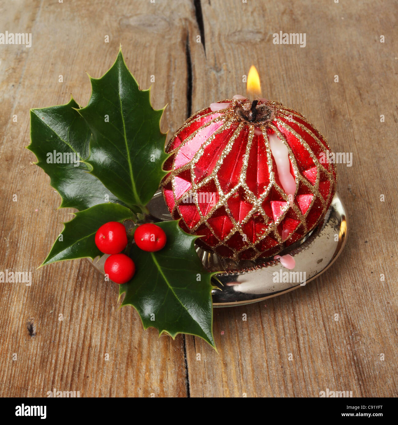 Dekorative brennende rote und Goldene Kerze mit einem Zweig frischer Holly auf einem Hintergrund von alten verwitterten Holz Stockfoto