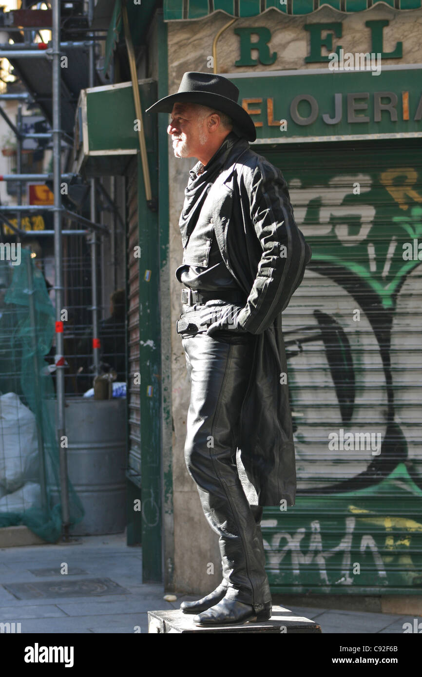 Streetart-Künstler gekleidet als Western Cowboy in schwarzem Leder mit einem schwarzen Fedora und Nachahmung Handfeuerwaffe vor einem graffitied Stockfoto
