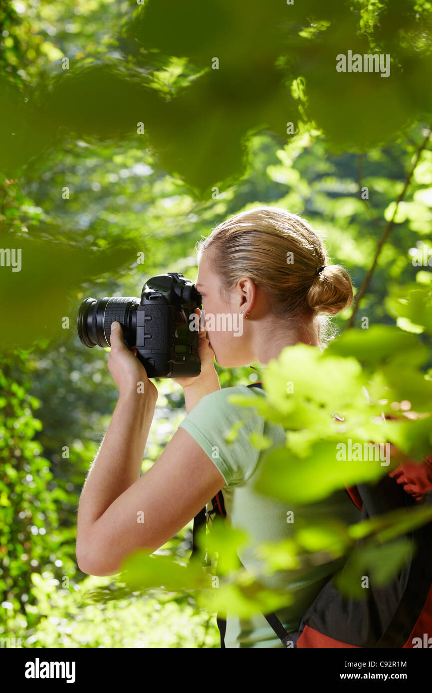 junge Frau trekking zwischen Bäumen und Fotografieren mit Dslr-Kamera. Vertikale Form, Seitenansicht, Hüfte aufwärts Textfreiraum Stockfoto