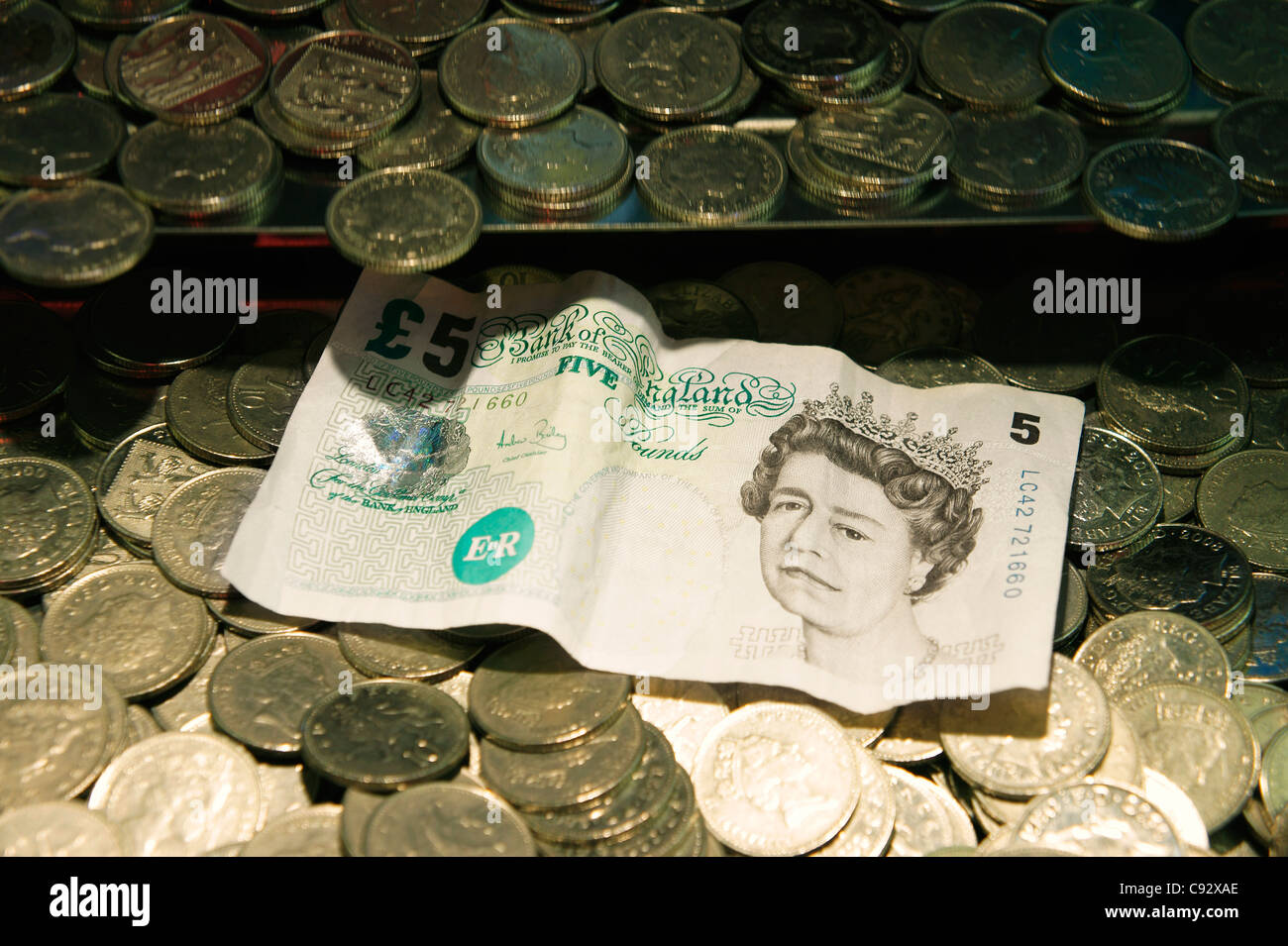 Bewusste Fokussierung. UK-Münzen und Queen es Kopf fünf-Pfund-Banknote. Seaside Spielhalle fällt Penny Spielautomaten Stockfoto