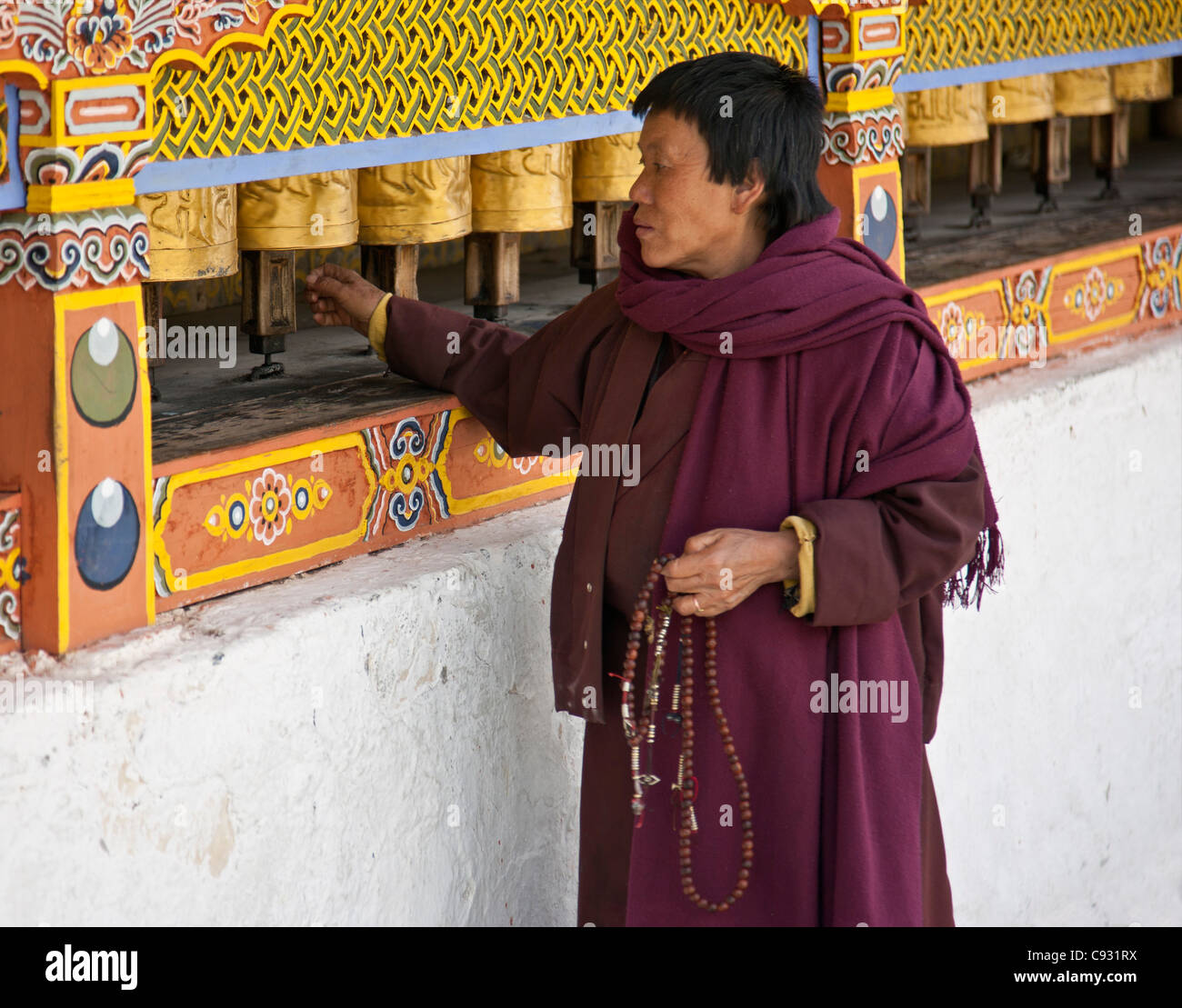 Eine Frau, Gebetskette in der Hand, dreht Messing Gebetsmühlen im 18. Jahrhundert Chorten Kora in Trashi Yangtze. Stockfoto