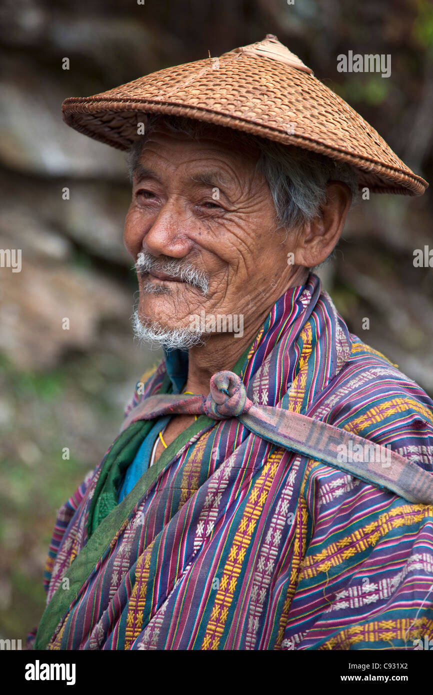 Ein runzligen alten Bauern in der Nähe von Mongar trägt die knielangen nationalen Robe Gho und eine konische Bambushut, das Belo genannt. Stockfoto