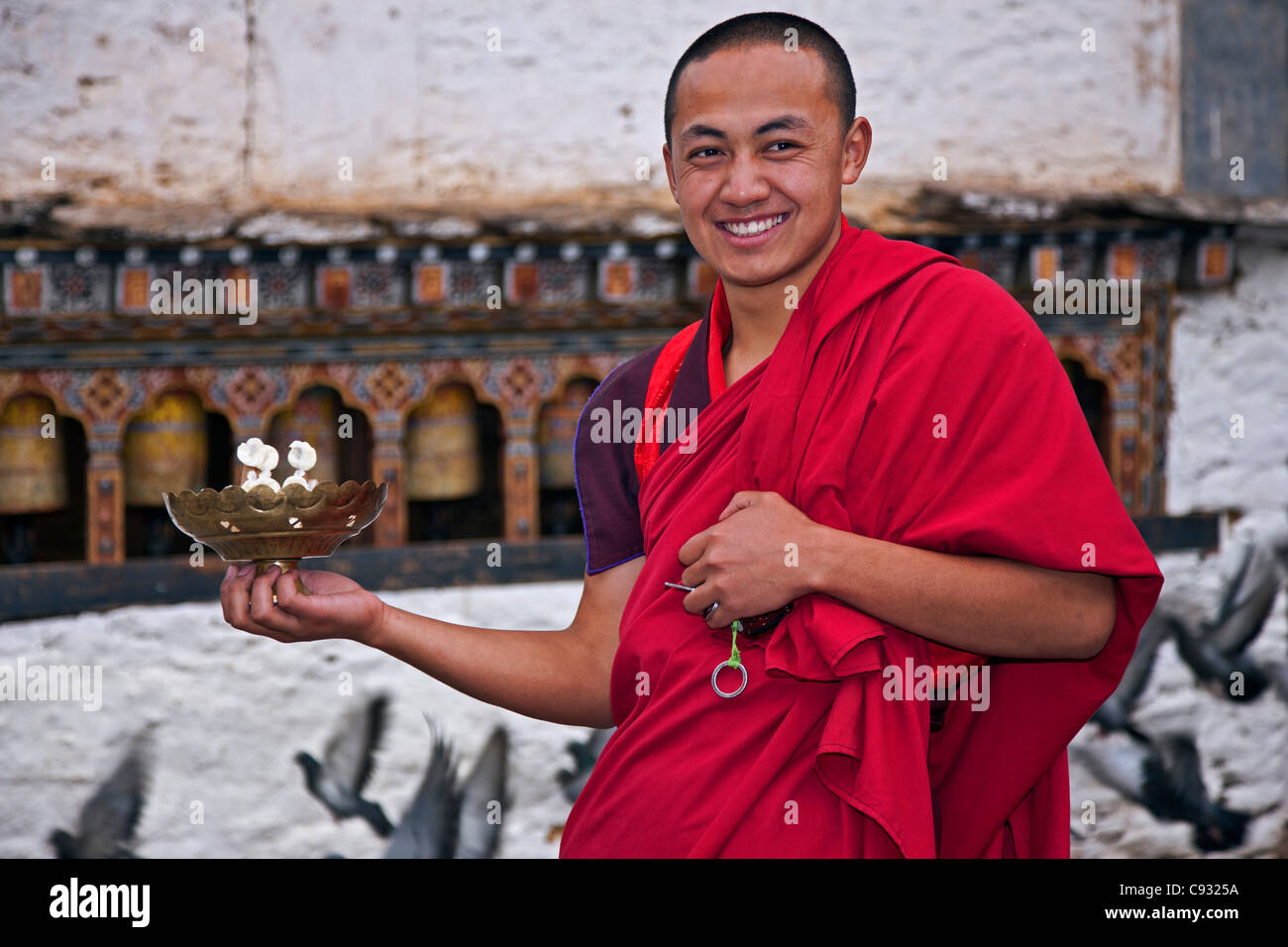 Jovialer Mönch führt rituelle Kuchen und Butter in eine Schüssel Messing als symbolische Opfergabe zu Gottheiten in Trongsa Dzong. Stockfoto