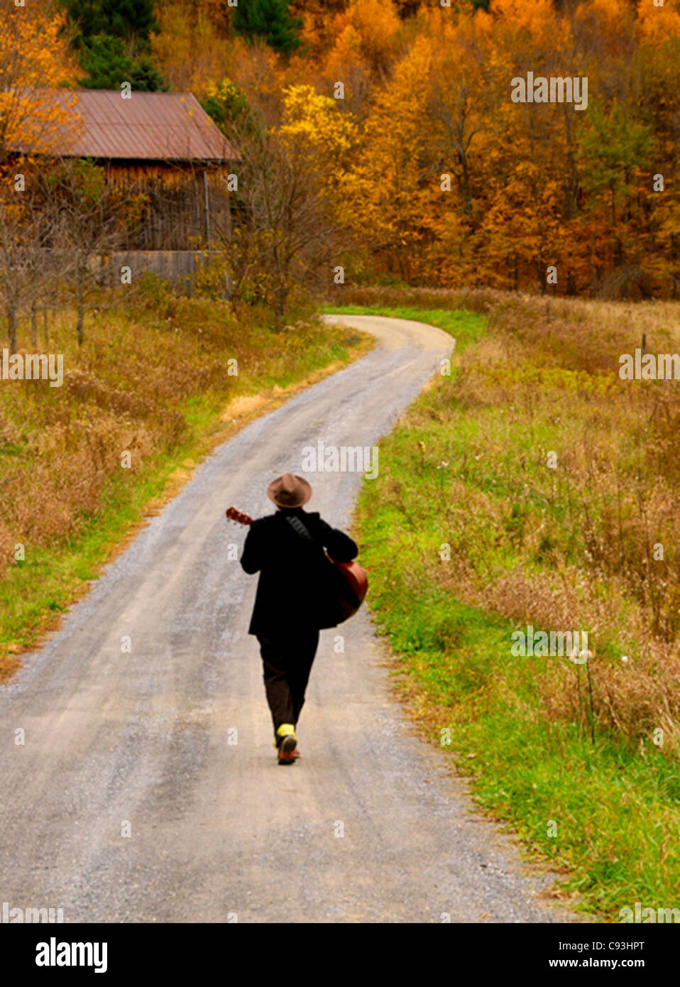 Mann zu Fuß auf Vermont Landstraße Gitarrenspiel von hinten, Michael Jermyn "The Minstrel', Herbst 2011 Stockfoto