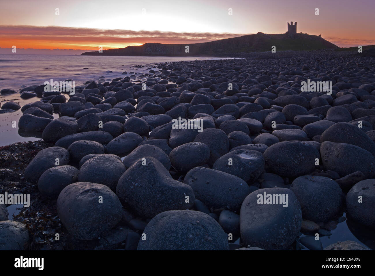 Sonnenaufgang am Dunstanburgh Castle, Northumberland, mit Felsvorsprüngen unten Stockfoto