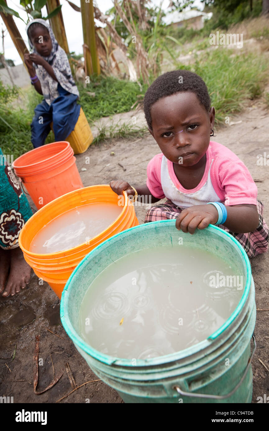 Ein Kind sitzt mit schmutzigem Wasser an einem Brunnen außerhalb Dar Es Salaam, Tansania, Ostafrika. Stockfoto