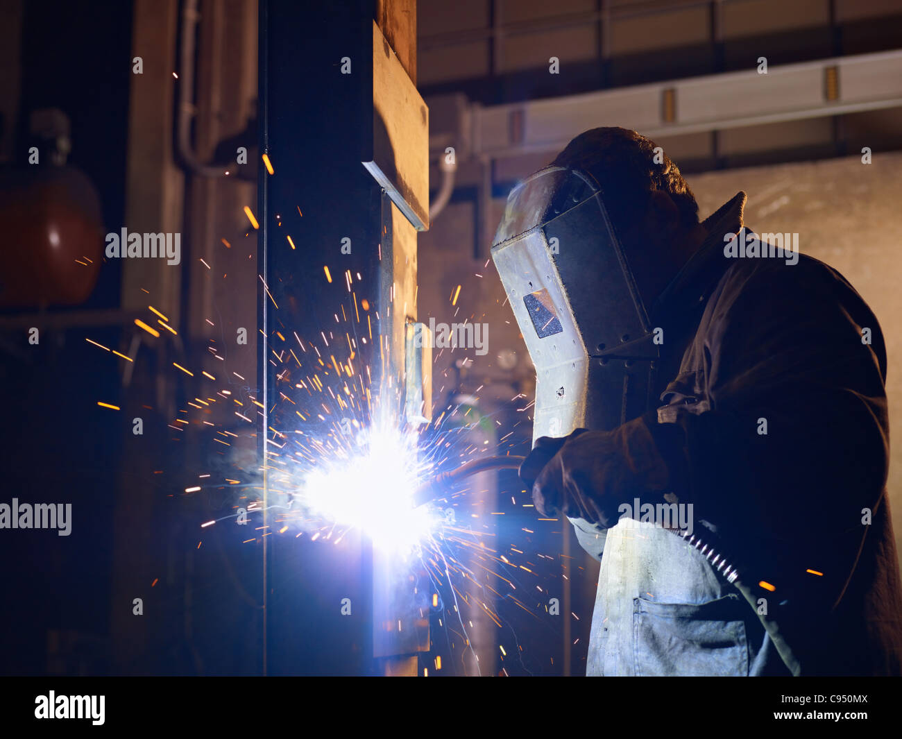 Arbeiter im Stahlwerk mit Schweißen Maske, Werkzeuge und Maschinen auf Metall. Horizontale Form, Seitenansicht, Hüfte aufwärts Stockfoto