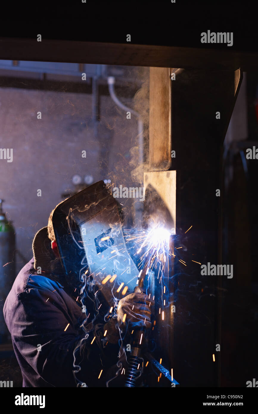 Arbeiter im Stahlwerk mit Schweißen Maske, Werkzeuge und Maschinen auf Metall. Vertikale Form, Seitenansicht, Textfreiraum Stockfoto