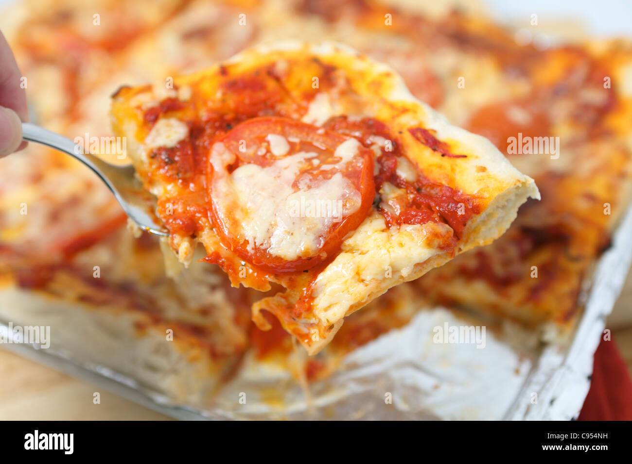 Ein Stück aus einer sizilianischen Stil rechteckige Käse und Tomaten Pizza, flache Tiefenschärfe geschnitten servieren. Stockfoto