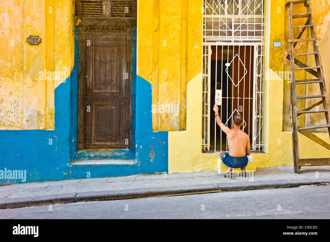 Ein Mensch malt das äußere seines Hauses in Havanna. Es dominieren helle Farben (blau, gelb und rosa). Stockfoto