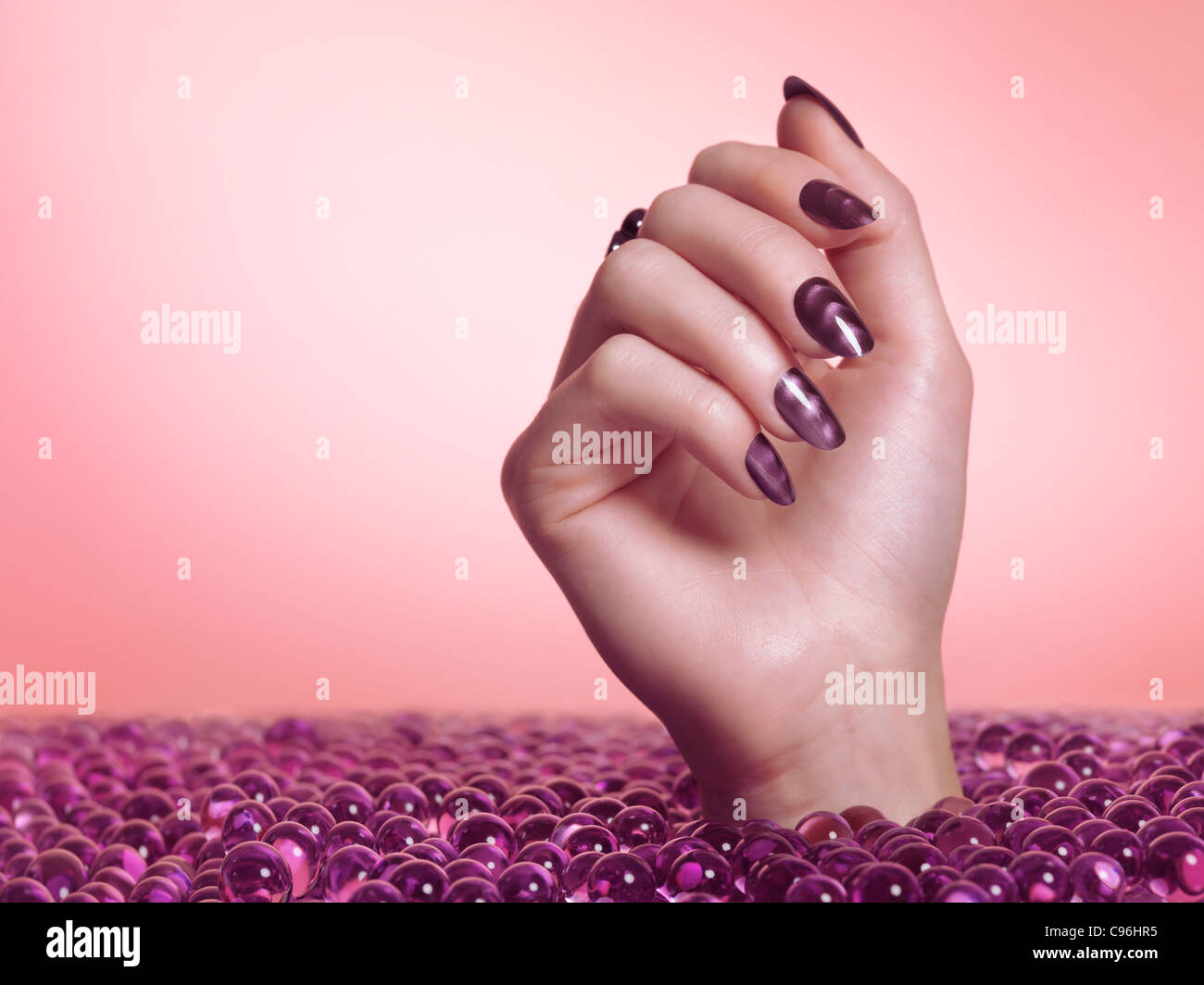 Lizenz erhältlich bei MaximImages.com Frauenhand mit lila nagellack aus einem Meer von Süßigkeiten auf rosa Hintergrund Stockfoto