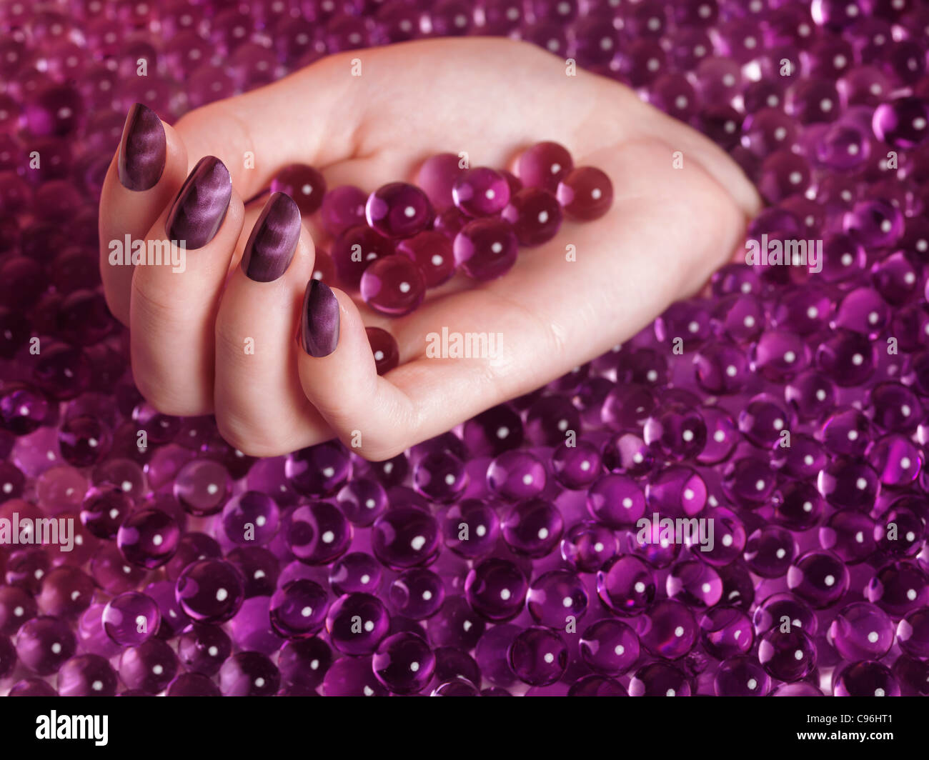 Lizenz erhältlich bei MaximImages.com Frauenhand mit violettem nagellack auf abstraktem rosa Süßwarenhintergrund Stockfoto