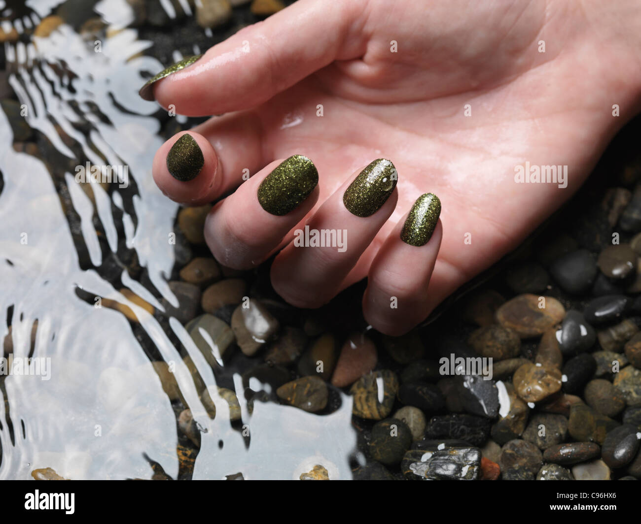 Lizenz erhältlich unter MaximImages.com Nahaufnahme der Frauenhand mit grünem, feinem nagellack im Wasser Stockfoto