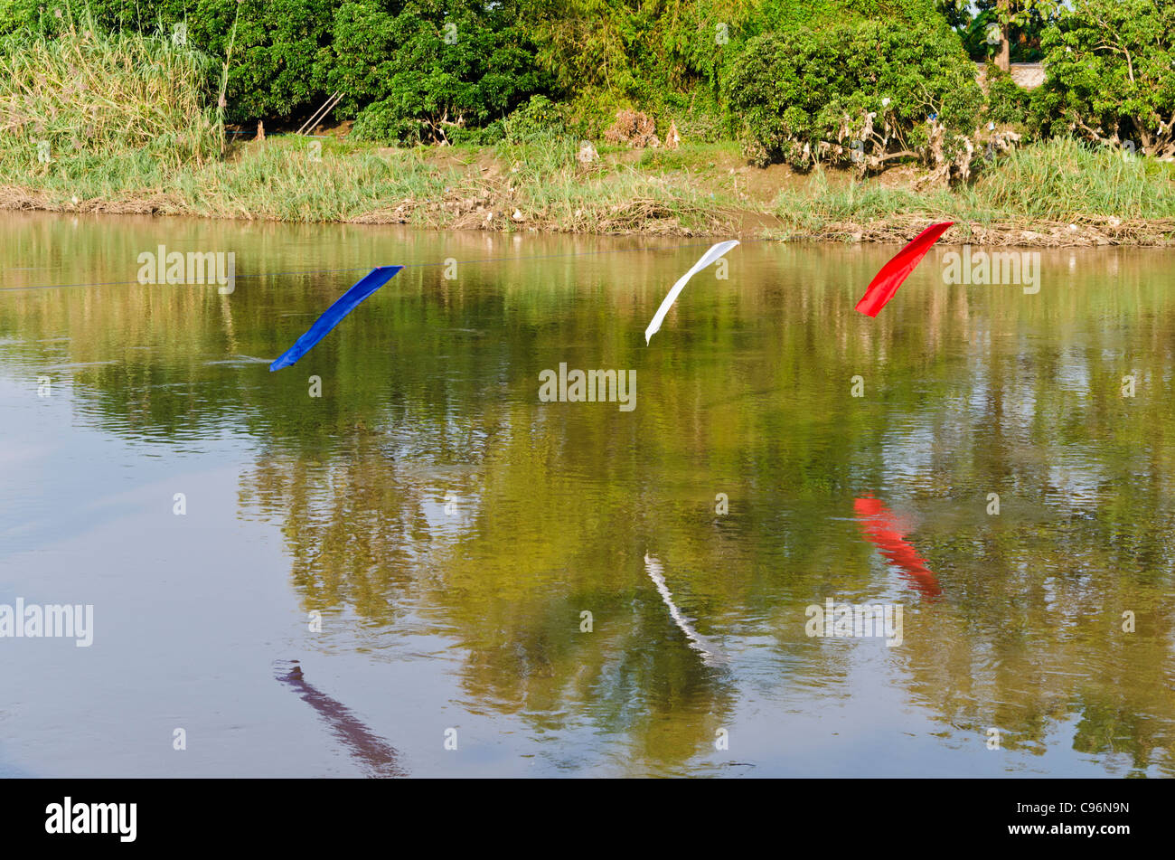 Drei roten weißen und blauen Banner aufgereiht über ruhige Fluss mit Reflexion in Nordthailand Stockfoto