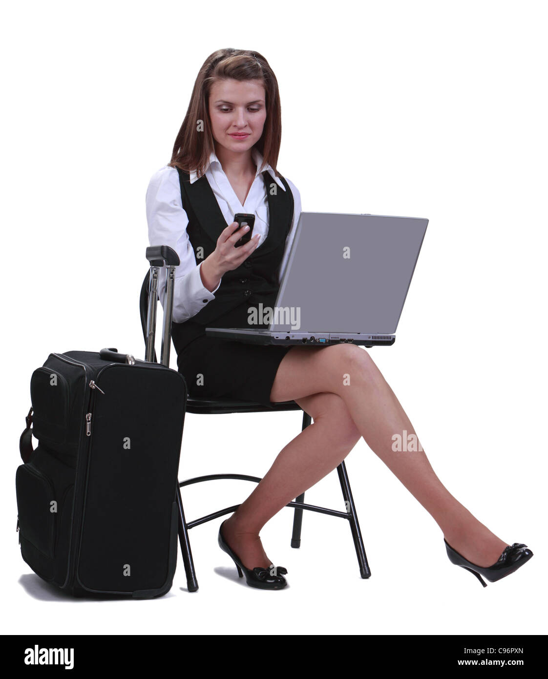Geschäftsfrau, die eine telefonische Nachricht zu lesen, während sie mit ihrem Laptop neben ihren Koffer, vor einem weißen Hintergrund sitzt Stockfoto