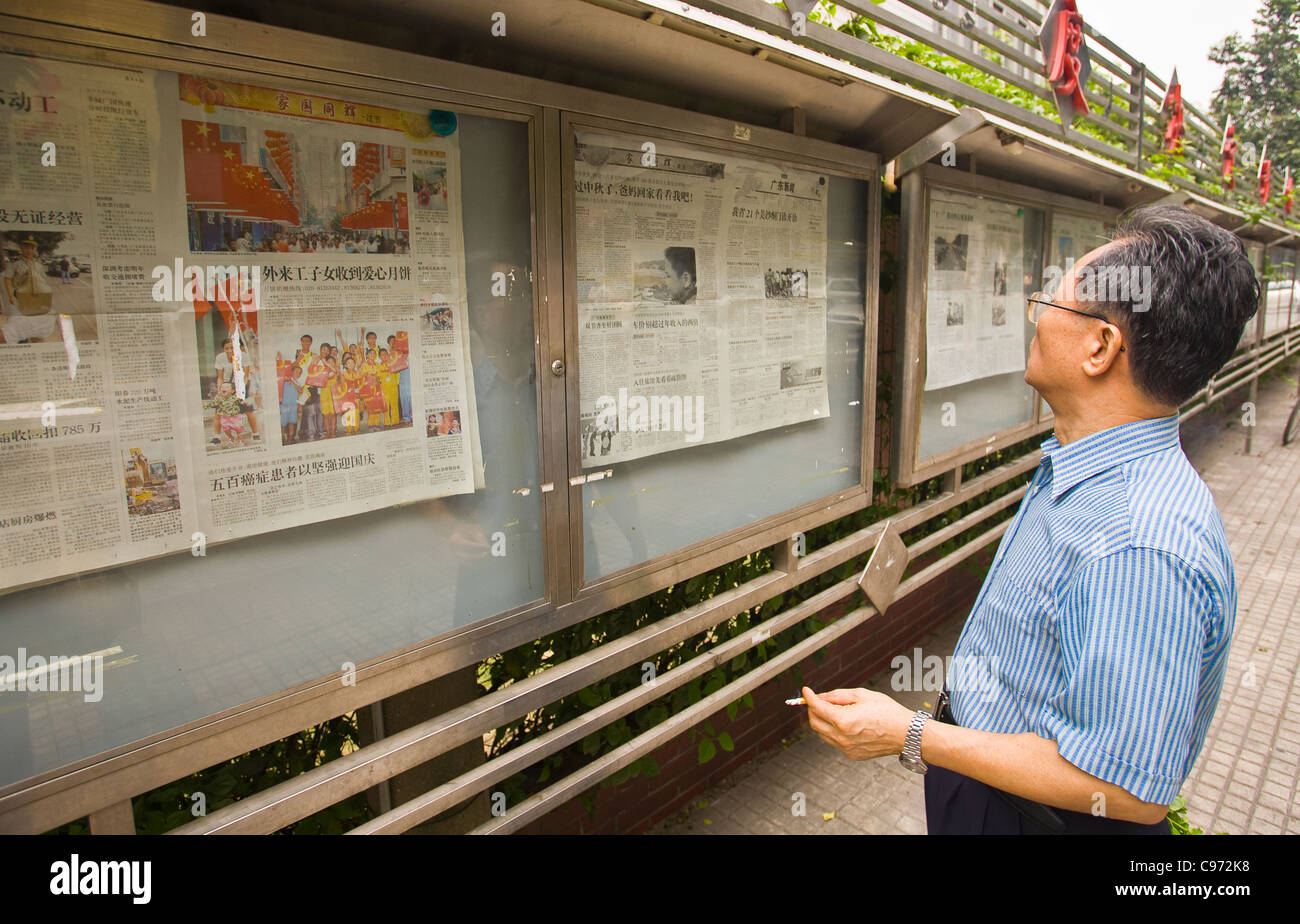 GUANGZHOU, Provinz GUANGDONG, CHINA - Mann lesen Zeitungen veröffentlicht in der Öffentlichkeit Vitrine auf Bürgersteig in Stadt Guangzhou Stockfoto