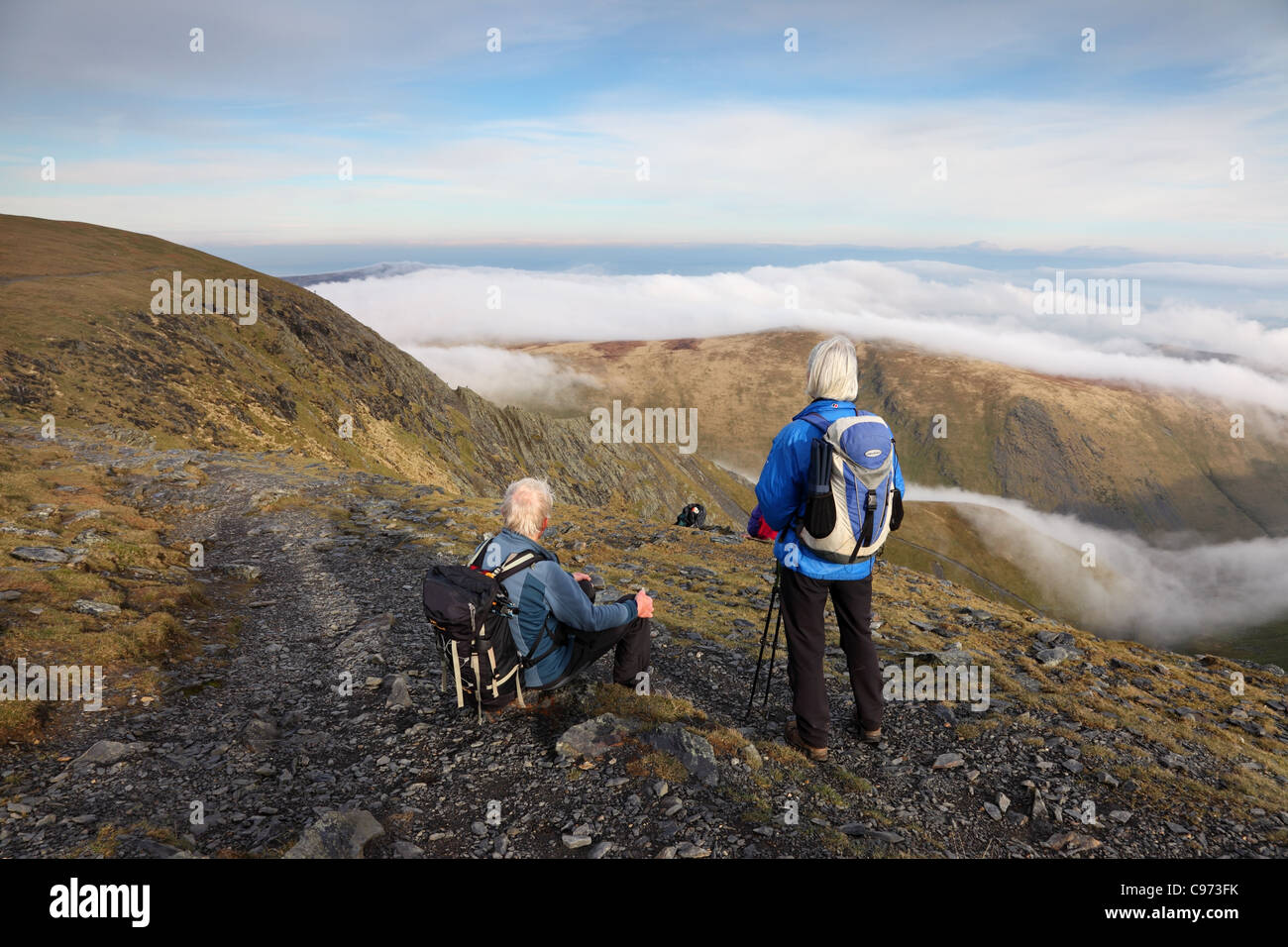 Zwei Wanderer beobachten Menschen kriechen entlang Sharp Edge auf Blencathra mit Wolken unter Seenplatte Cumbria UK Stockfoto