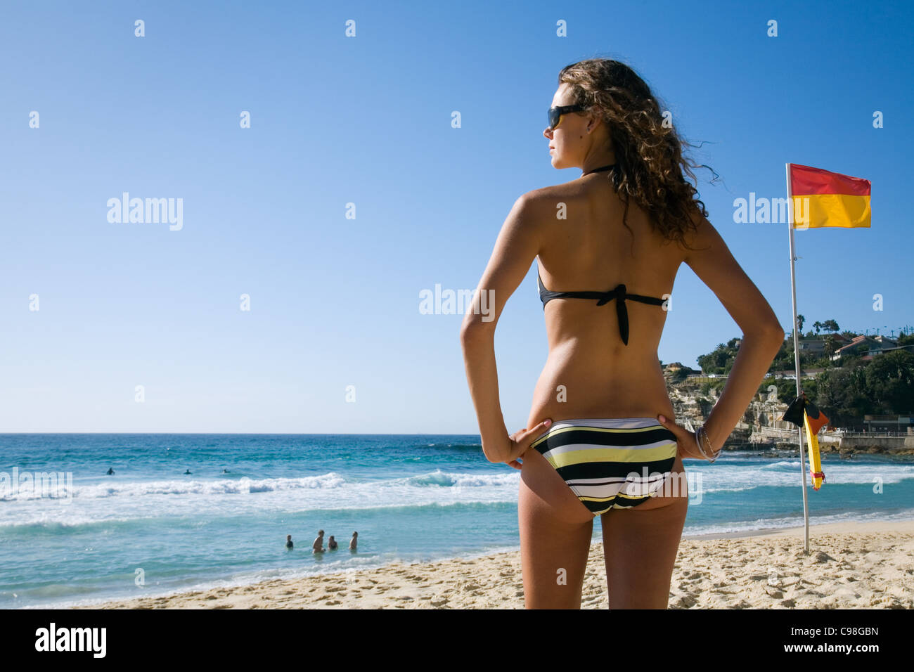 Frau im Bikini stehen neben roten und gelben Surf Lifesaving Flagge am Strand. Sydney, New South Wales, Australien Stockfoto