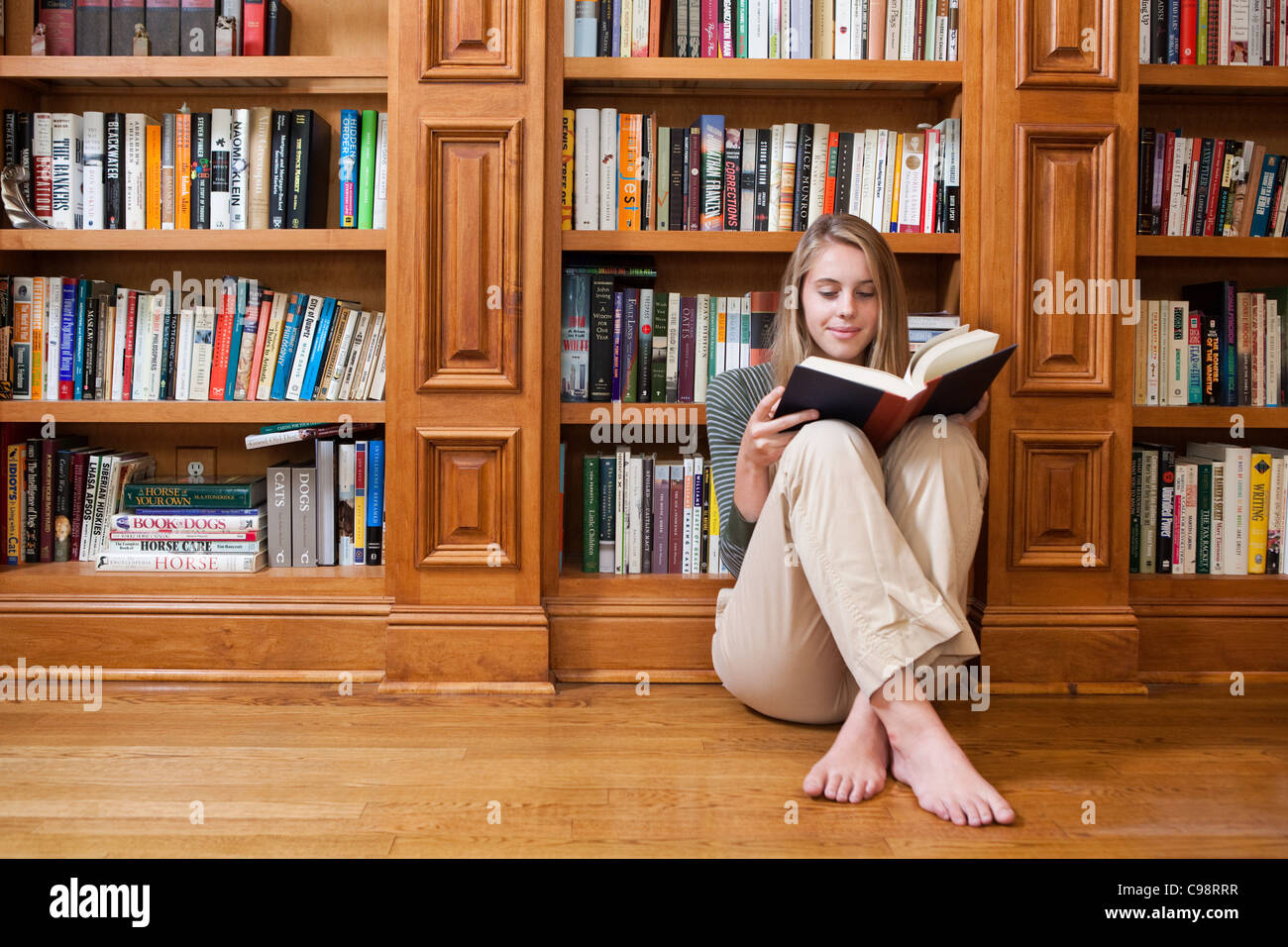 Junge Frau, die Lesung am Boden durch Bücherregale Stockfoto