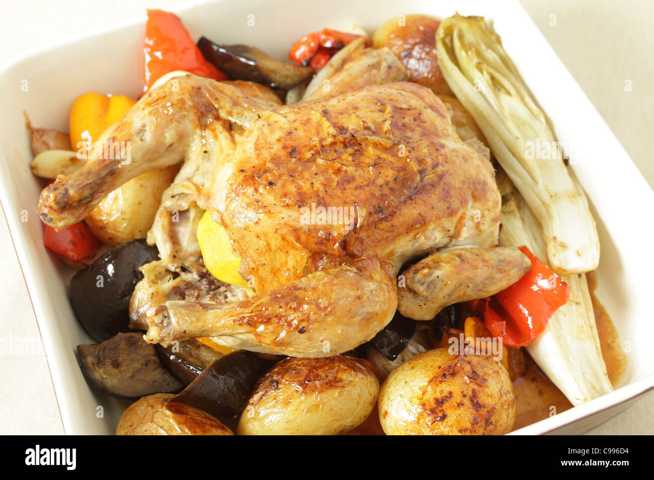 Gebratenes Huhn in einer Schüssel auf einem Bett von Ofen gebraten Gemüse einschließlich Kartoffeln, Paprika, Chicorée, Auberginen und Knoblauch. Stockfoto