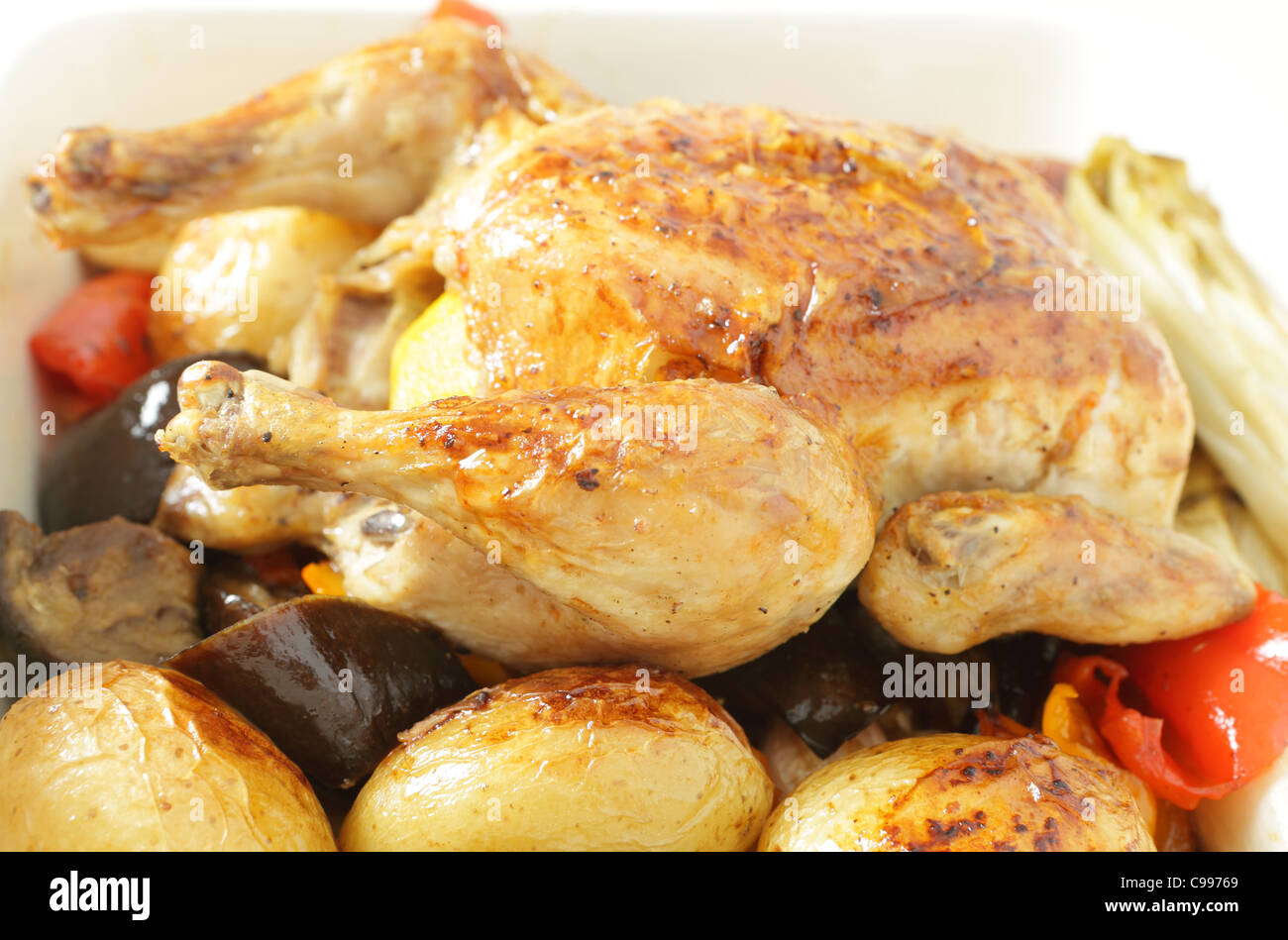 Gebratenes Huhn in einer Schüssel auf einem Bett von Ofen gebraten Gemüse einschließlich Kartoffeln, Paprika, Chicorée, Auberginen und Knoblauch. Stockfoto