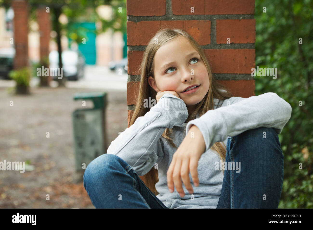 Deutschland, Berlin, Mädchen sitzen vor roten Backsteinmauer Stockfoto