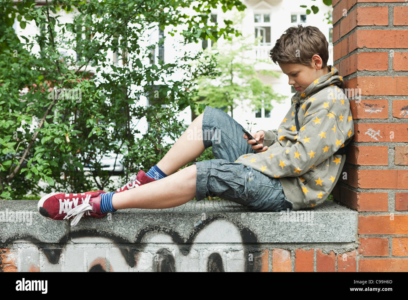 Deutschland, Berlin, junge saß gegen Mauer mit Handy Stockfoto