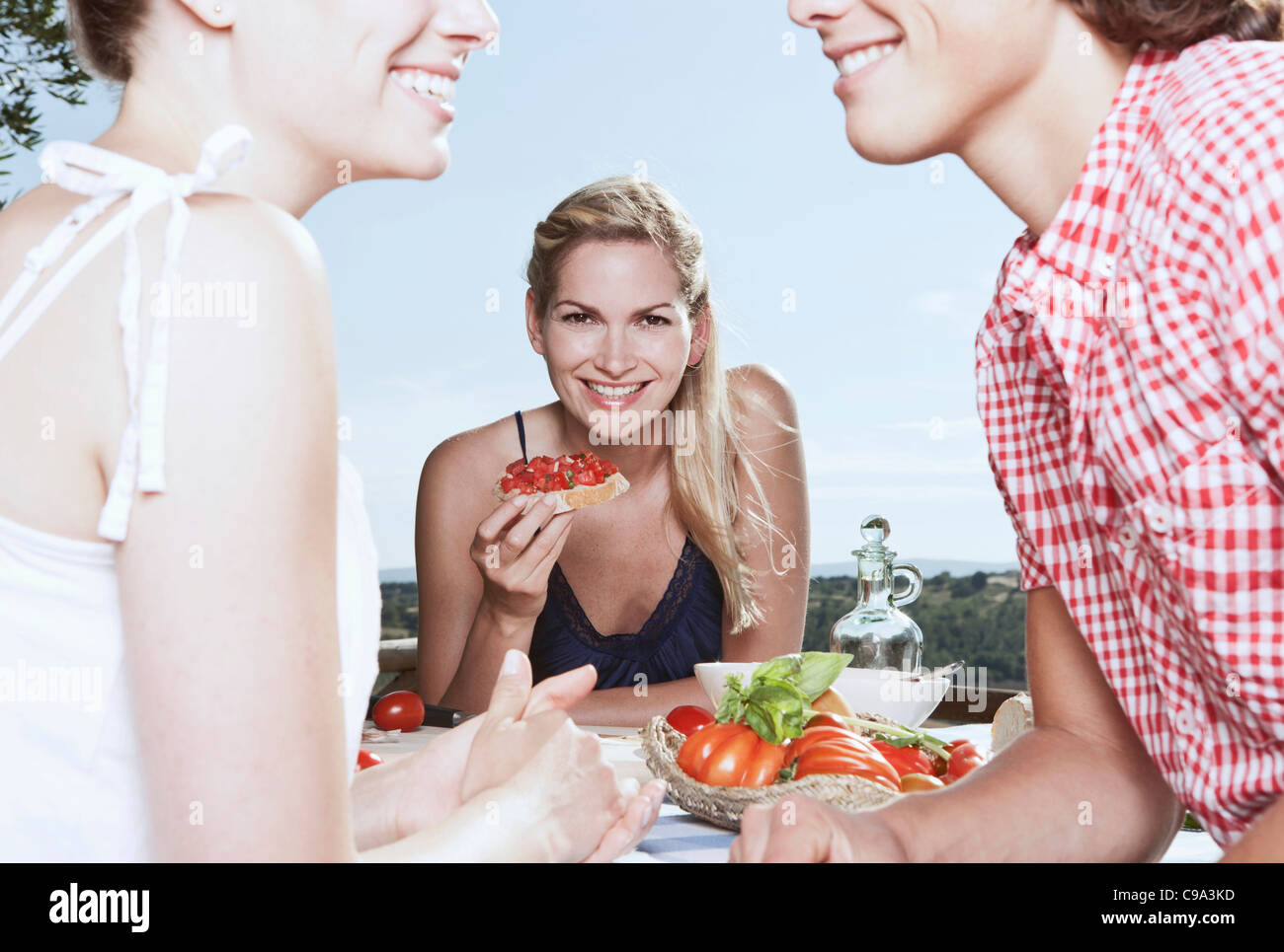 Italien, Toskana, Magliano, junge Frau halten Essen und Freunde im Vordergrund, Lächeln Stockfoto