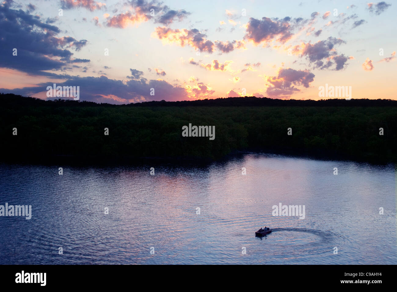 Sonnenuntergang über einem See mit Angelboot/Fischerboot im Vordergrund. Stockfoto