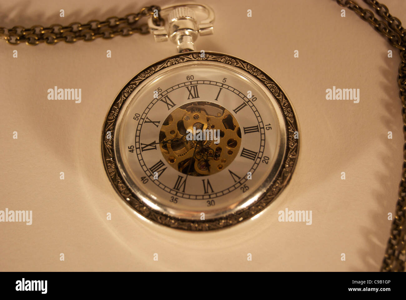 Eine Taschenuhr an einer Kette mit römischen Ziffern und Innenleben zeigt durch Ziffernblatt Stockfoto