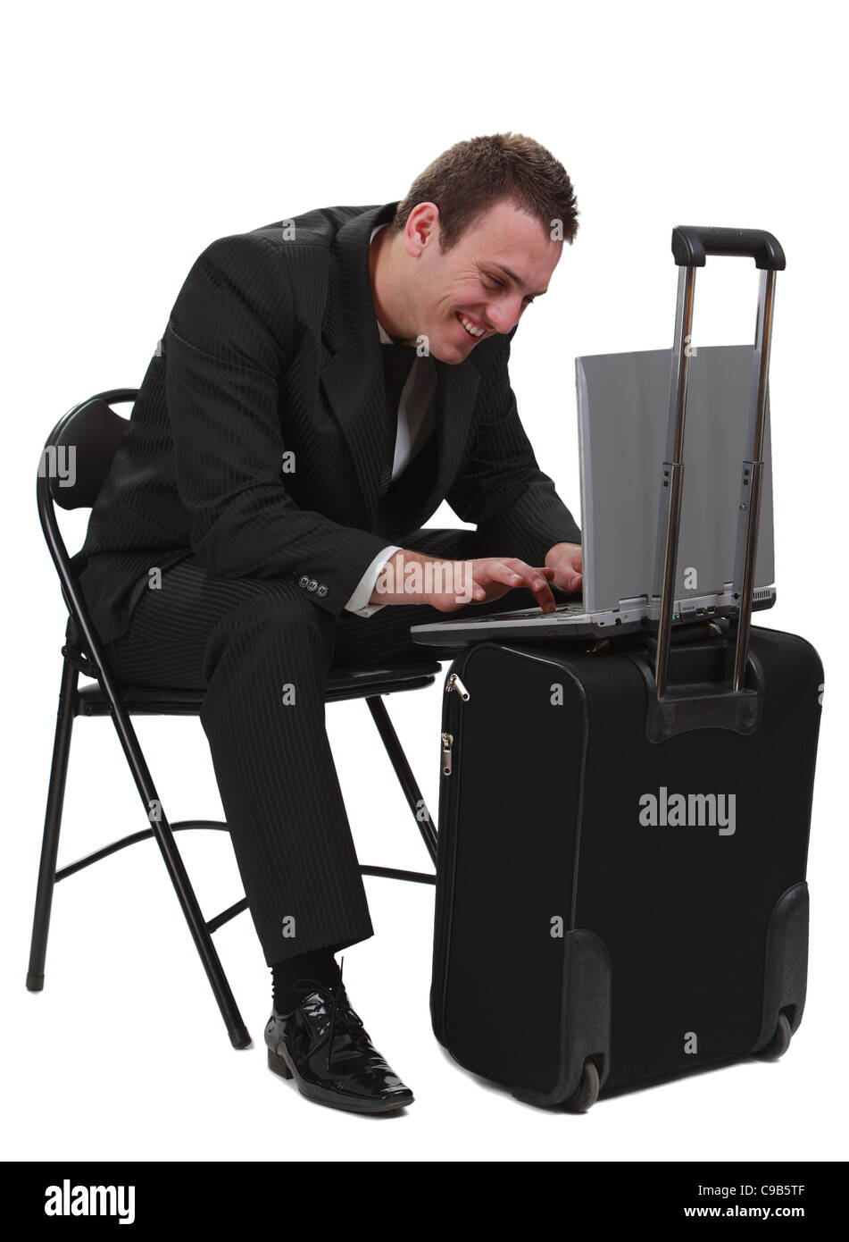Jungen lächelnden Mann Reisenden in Eile auf seinem Laptop auf einen Koffer-vor einem weißen Hintergrund isoliert arbeiten. Stockfoto